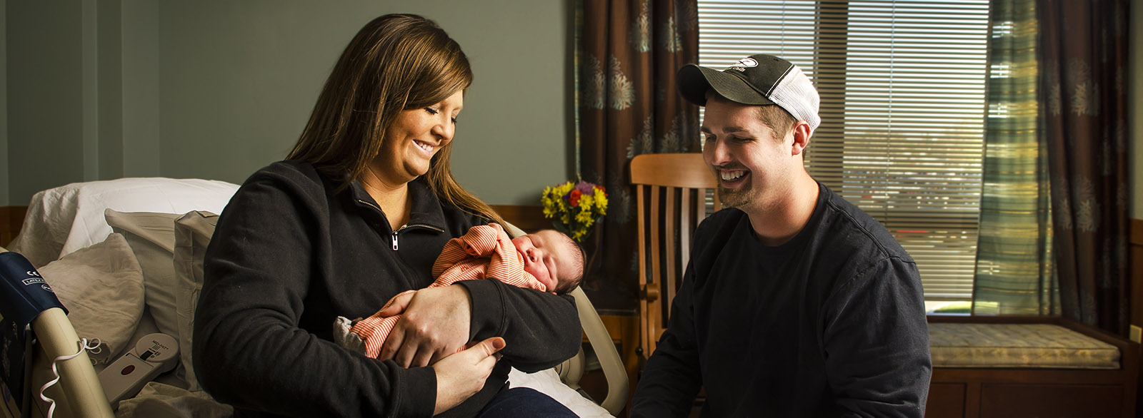 New mother holding her baby with husband nearby in the Birthing Center at Columbus Regional Health.