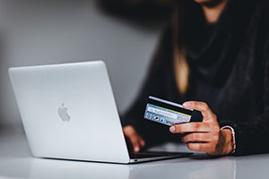 paperless-billing Hand holding credit card beside laptop computer.
