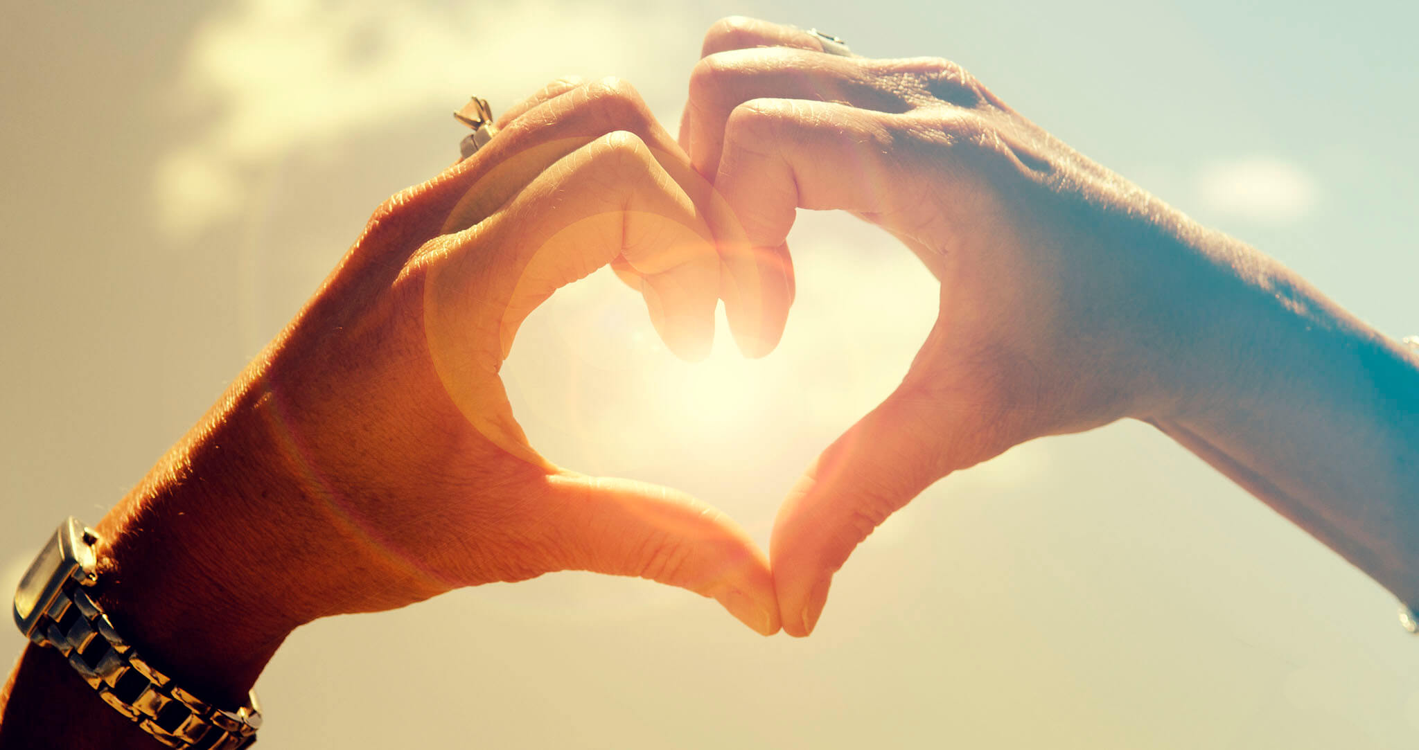 Hands forming a heart with sun in background
